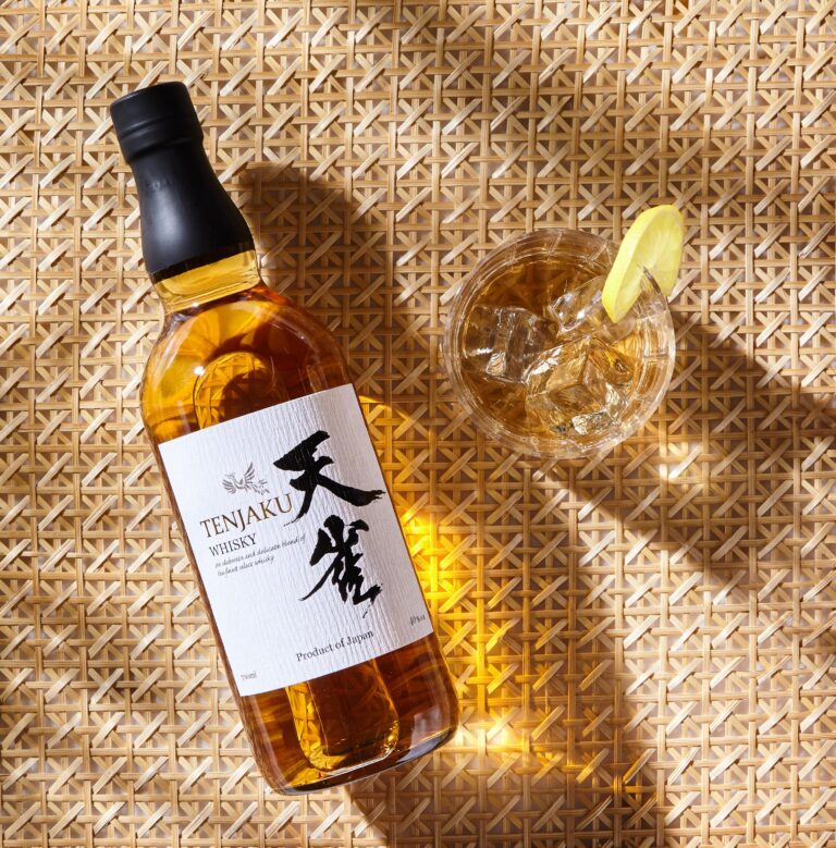 Tenjaku Whisky bottle beside an iced drink with lemon on woven matting.
