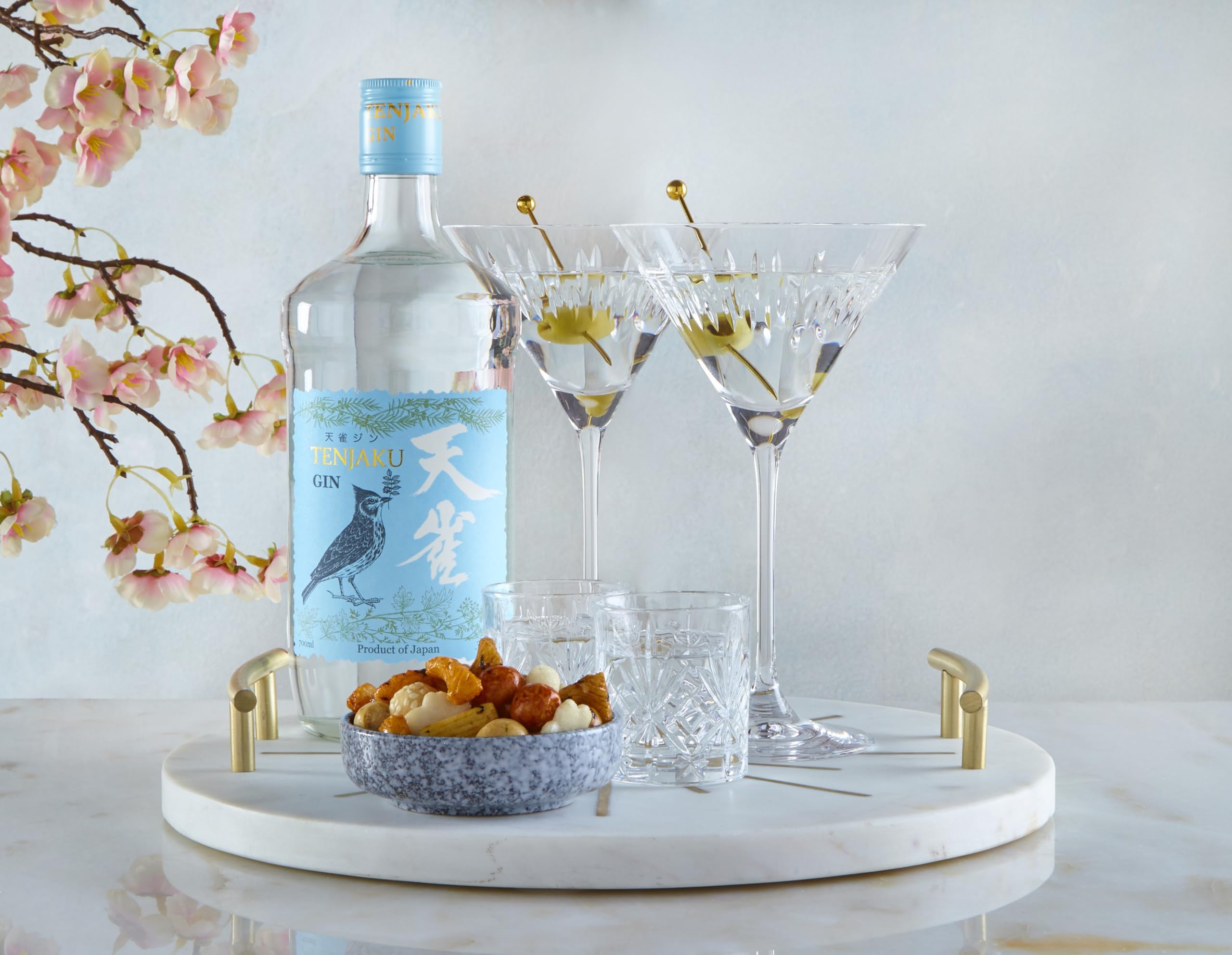 Tenjaku Gin bottle with two cocktails, cut-glass tumblers and pink blossoms.