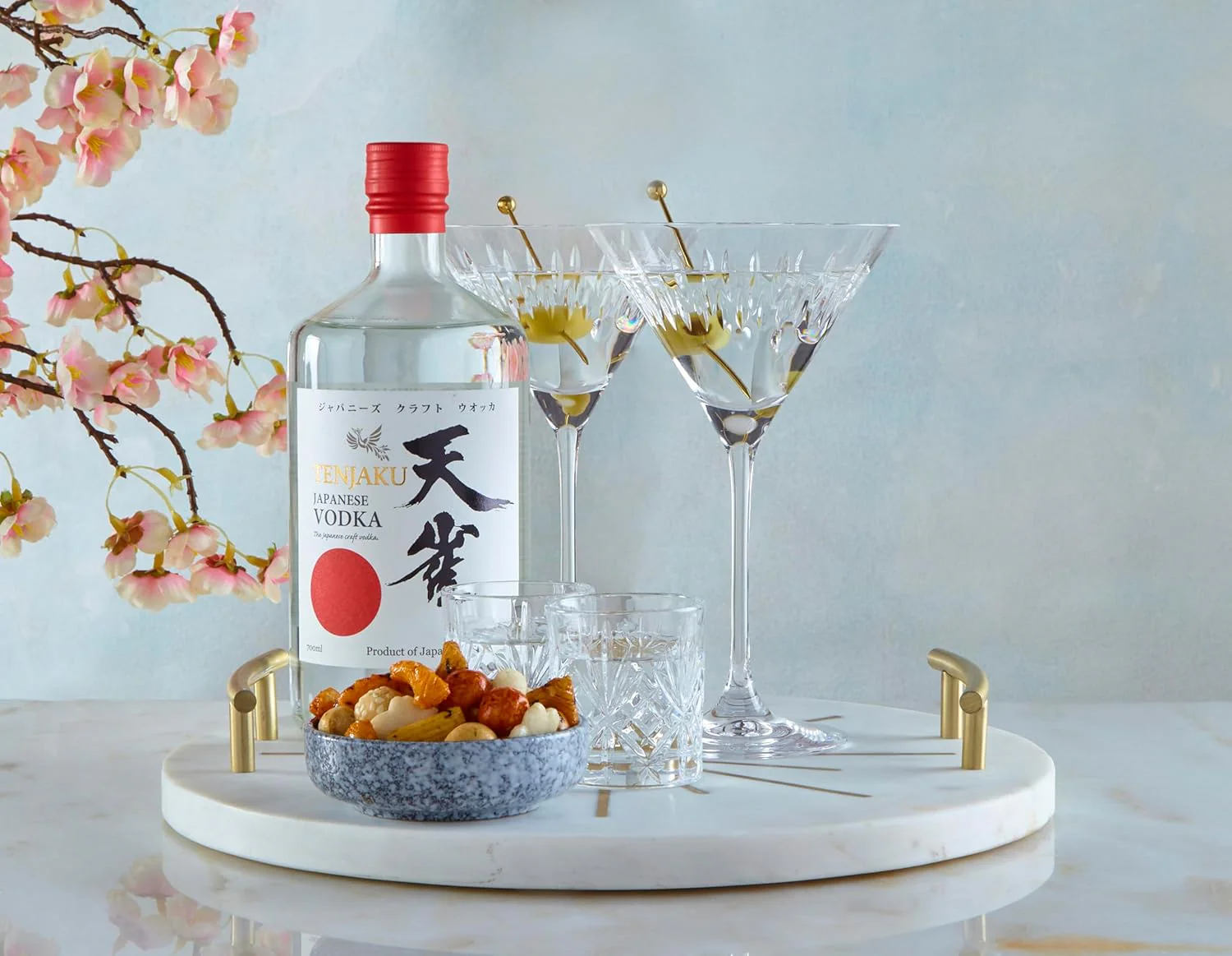 Bottle of TENJAKU Vodka displayed on a white tray with cocktail glasses, glassware, blossoms and decorative elements.